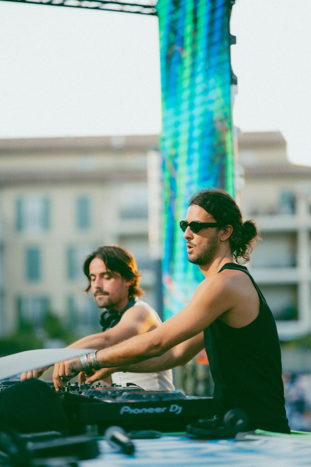 Two DJs performing at outdoor festival using Pioneer DJ equipment with colorful tower backdrop.