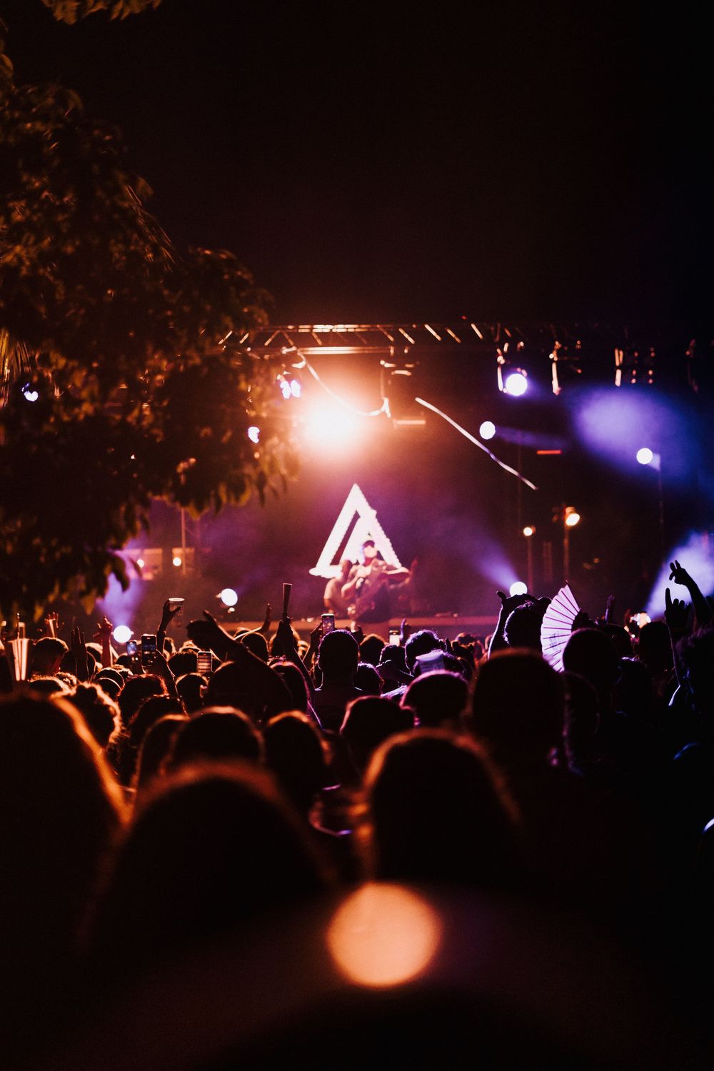 Crowd at an outdoor night concert with glowing stage lights and a triangle backdrop illuminating the performer.