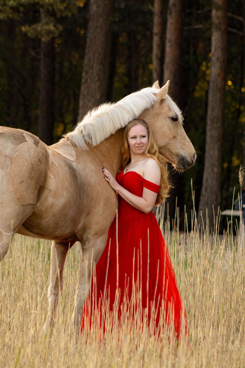 Vrouw in een rode jurk met een lichtbruin paard, dat paard omhelst.