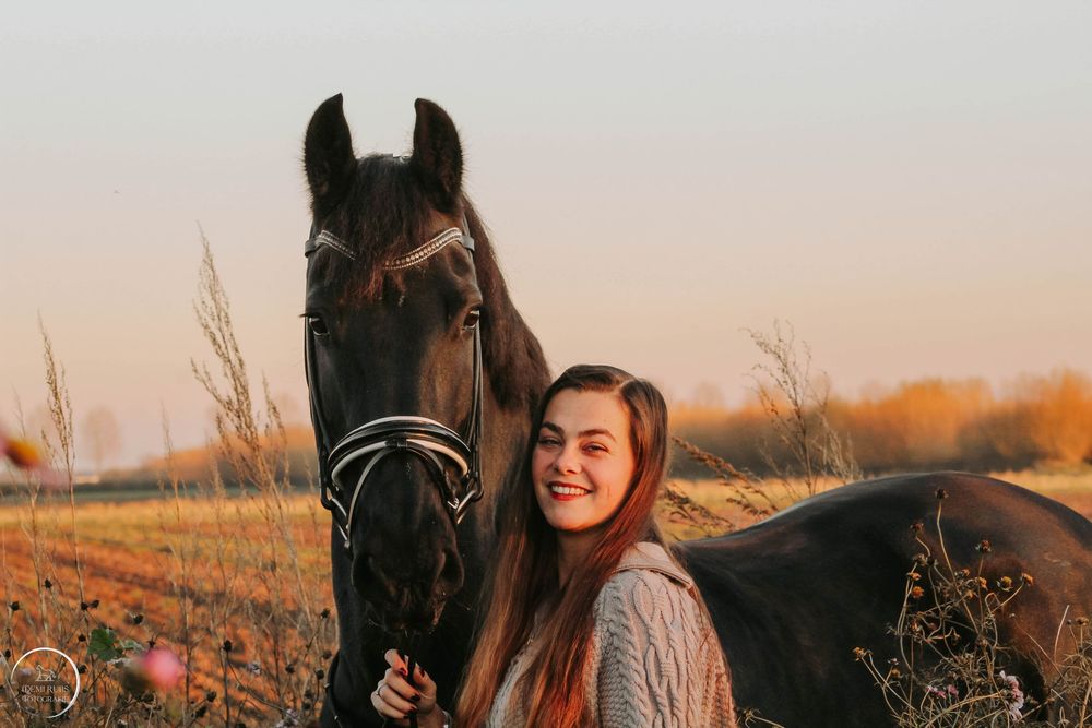 Jonge vrouw op zwart paard met zonsondergang.