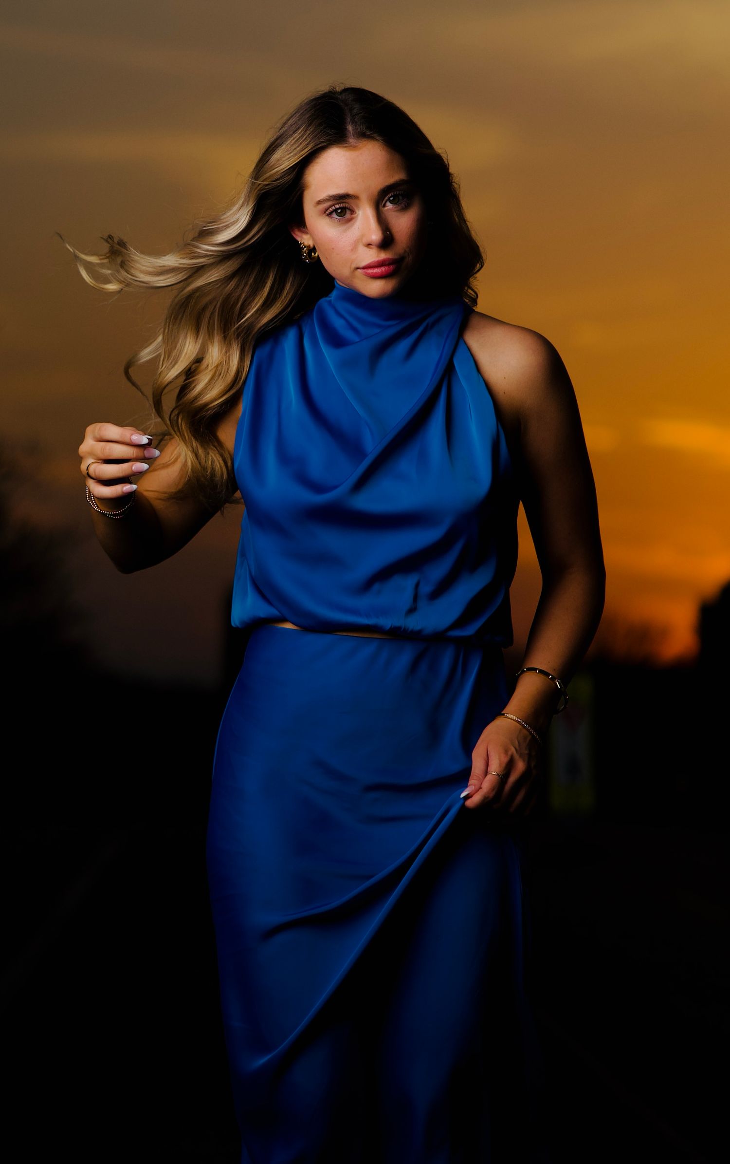 A figure in a flowing royal blue dress poses dramatically against a sunset sky in an artistic photo sequence.