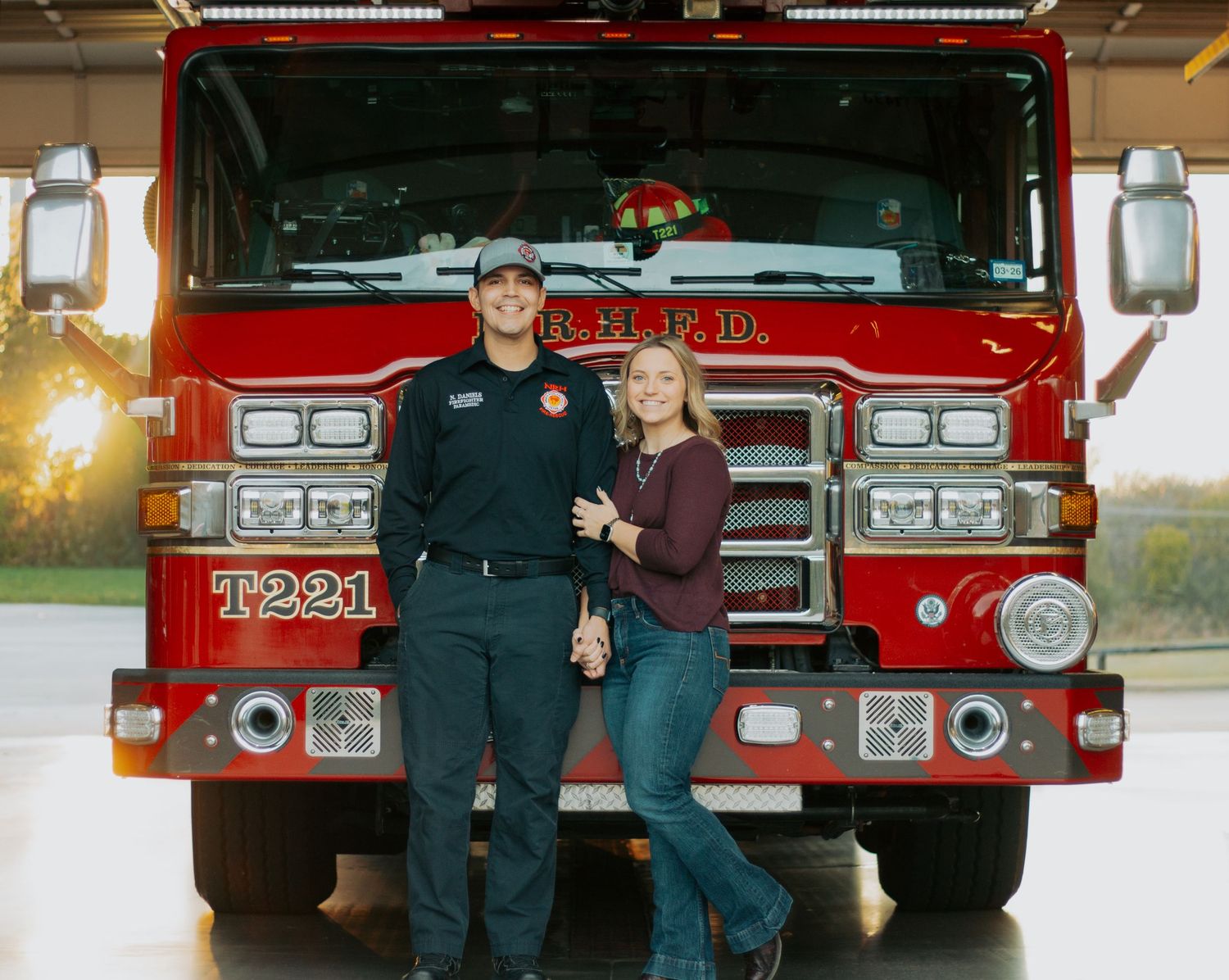 A couple poses in front of a vintage red fire truck for engagement photos at sunset.