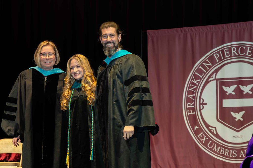 Three graduates smile while standing together at Franklin Pierce University's graduation ceremony.