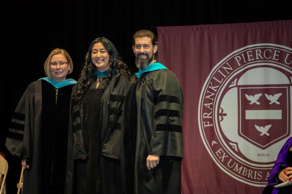 Three graduates in academic regalia stand together at a Franklin Pierce University graduation ceremony.
