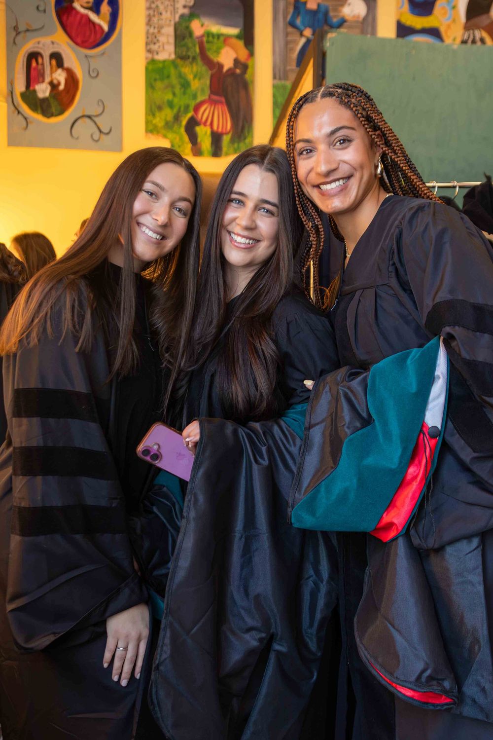 A group wearing graduation robes poses together in front of a colorful wall with artwork.
