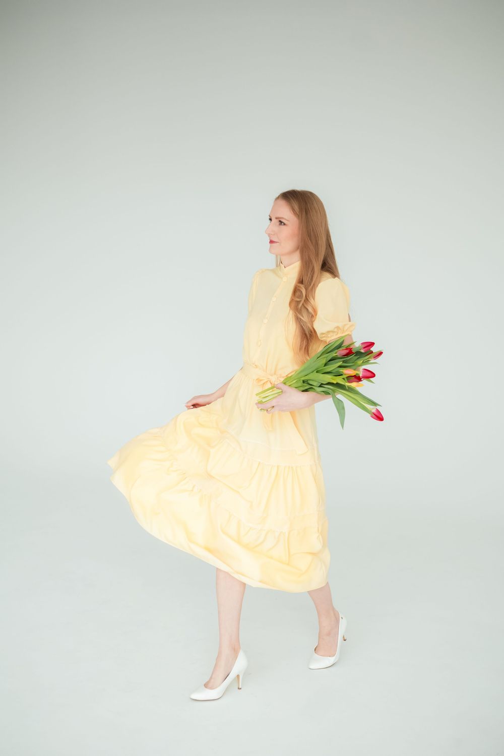 Mladá žena vo voľných žltých šatách s kyticou červených tulipánov v žiare štúdiových svetiel. Fotograf Žilina.