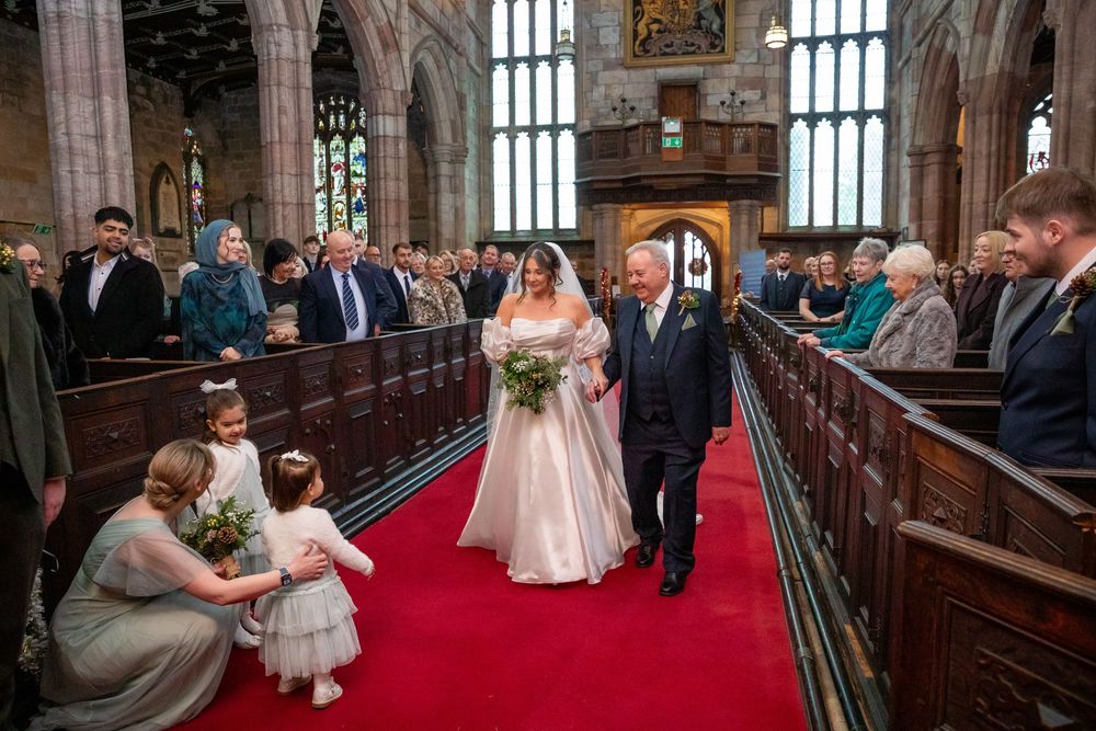 Bride walks down red carpet aisle with father in stunning historic church wedding ceremony.