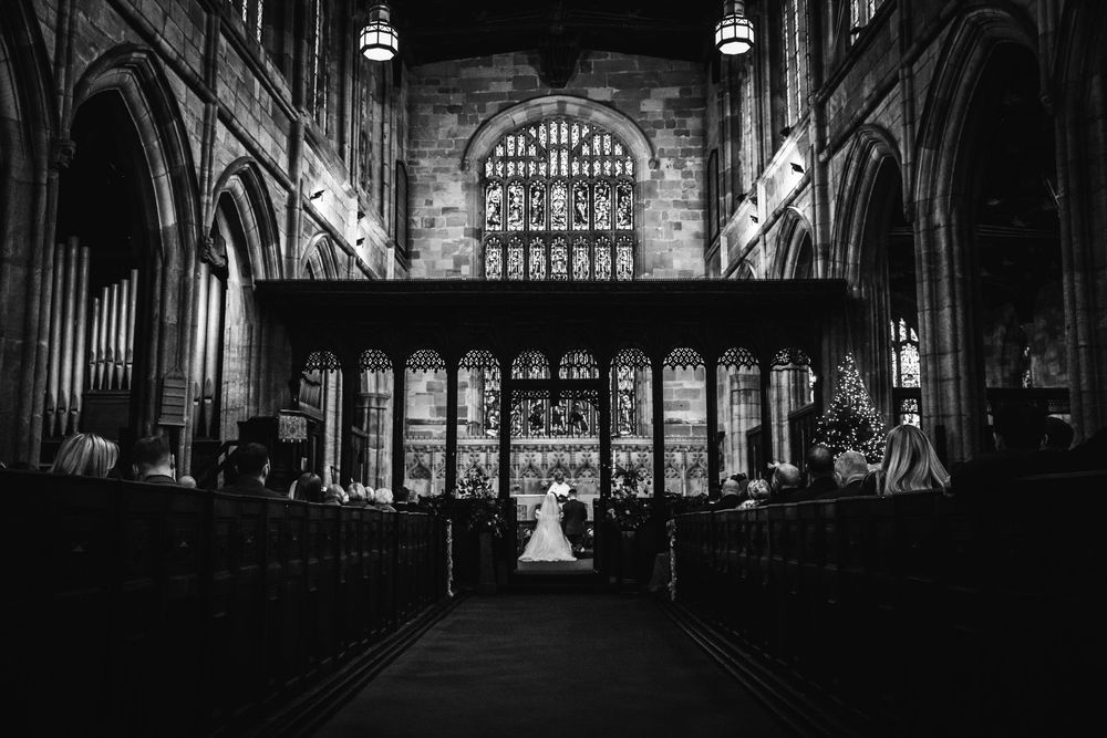 Black and white wide shot of bride and groom at altar in grand cathedral church.