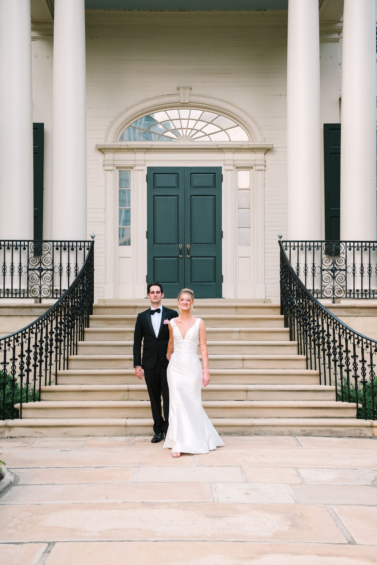 Classic wedding portrait on grand white building steps with ornate door and iron railings.