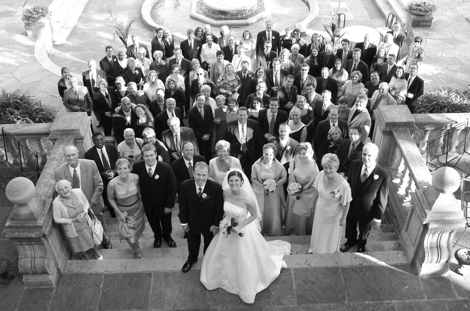 A black and white wedding photo showing a large group gathered on elegant stone steps.