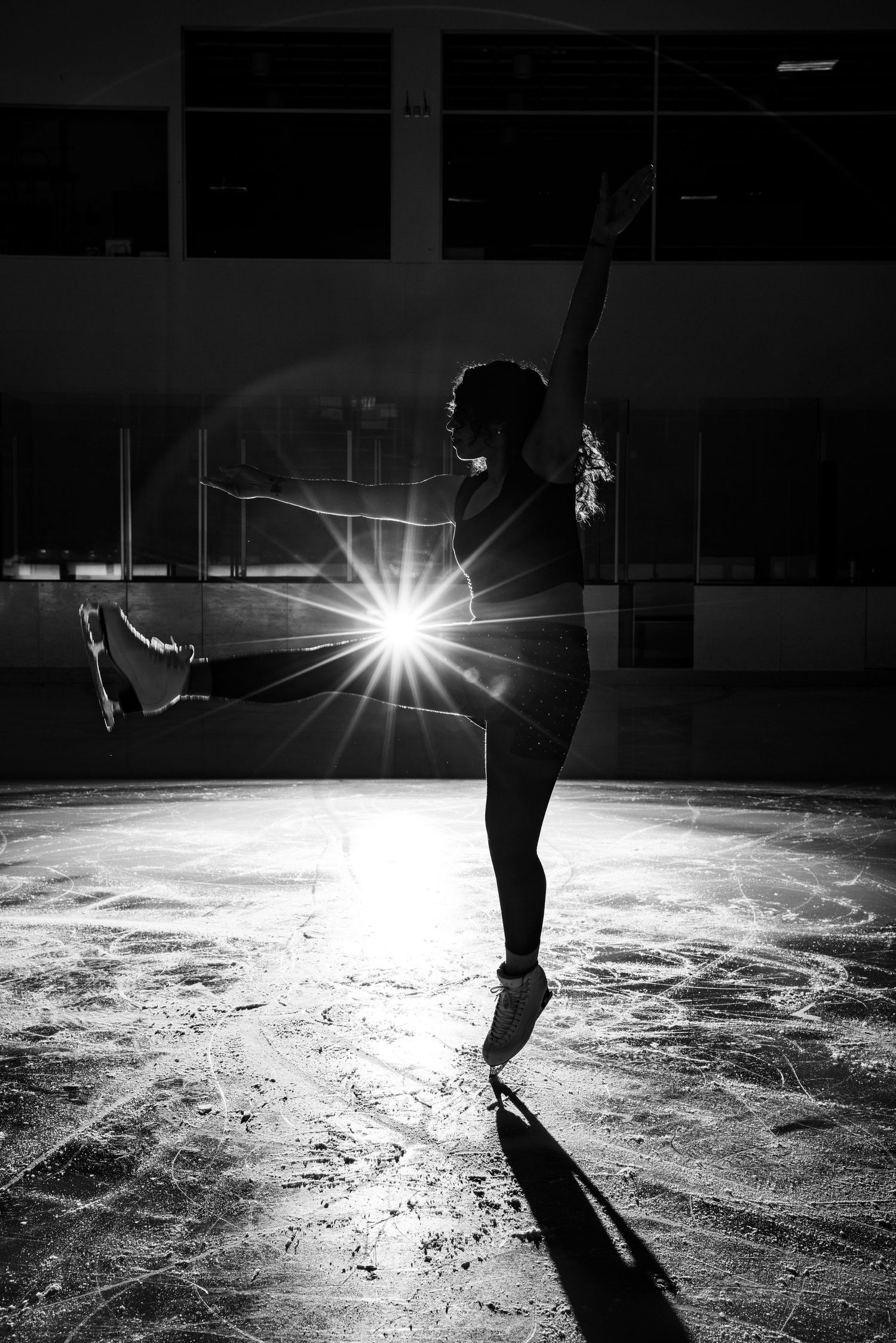 Dramatic black and white silhouette of female figure skater with starburst light effect on ice rink.