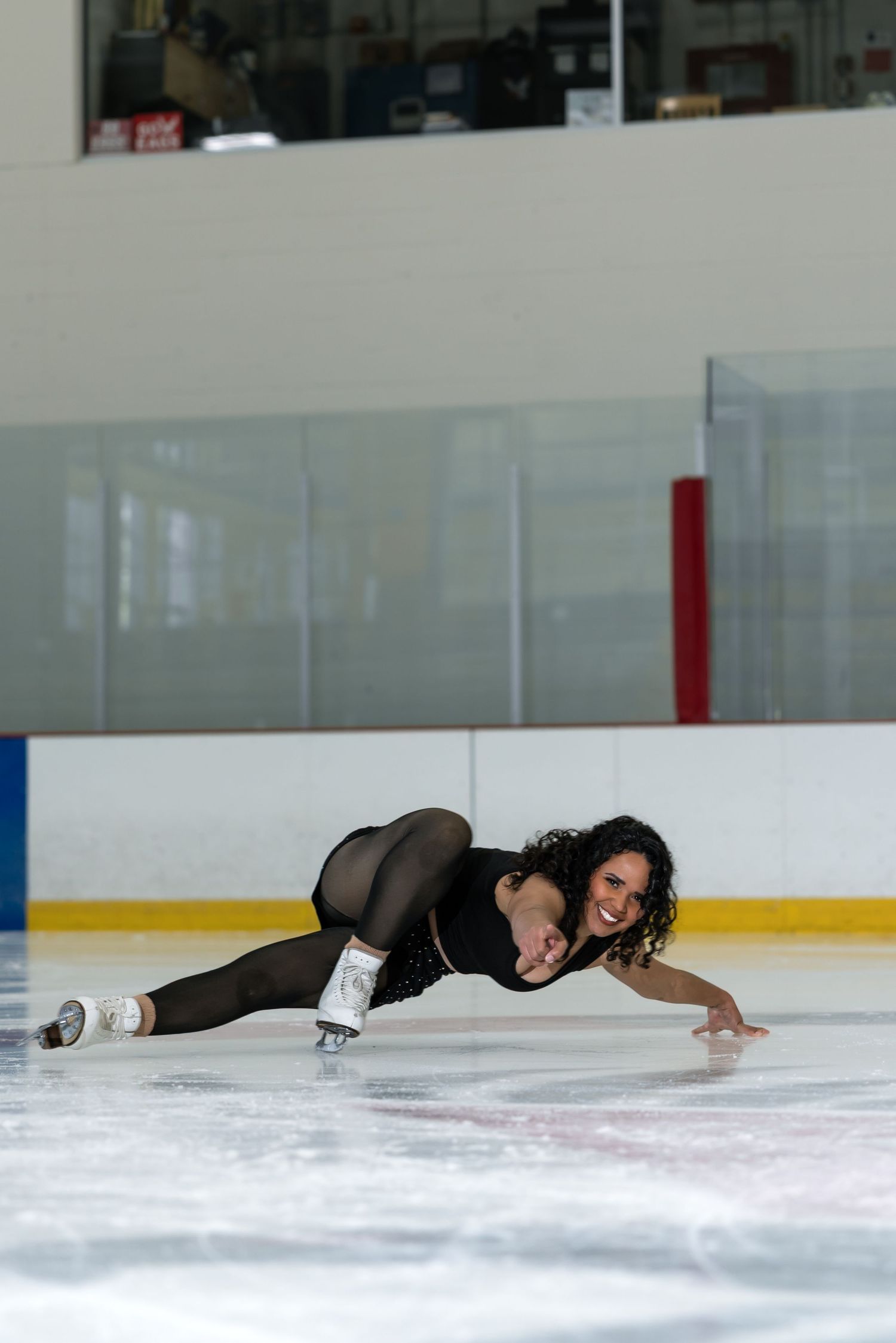 Female figure skater in black outfit performing a low spin move on indoor ice rink.