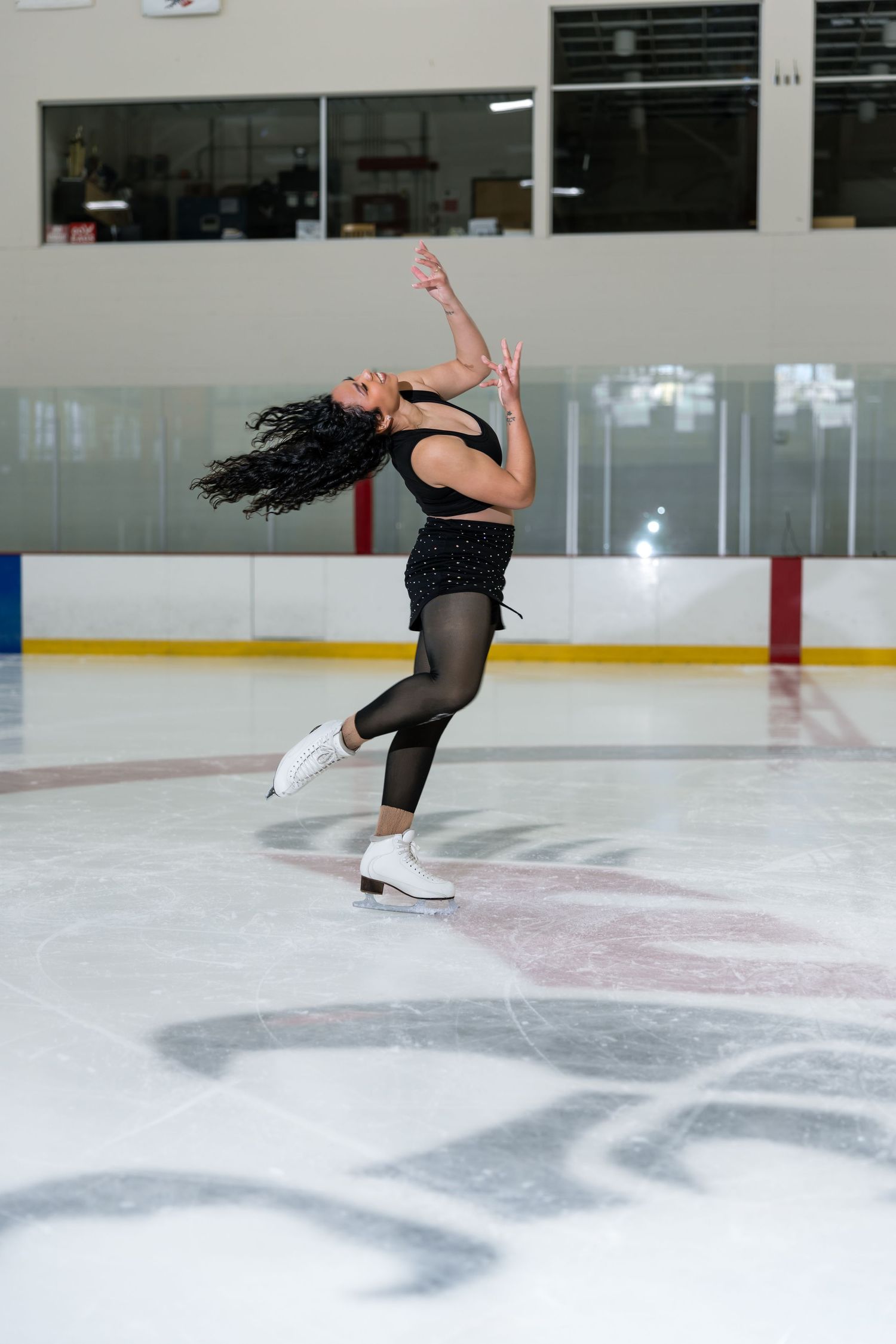 Female figure skater in black outfit performing graceful spin on indoor ice rink with white skates.
