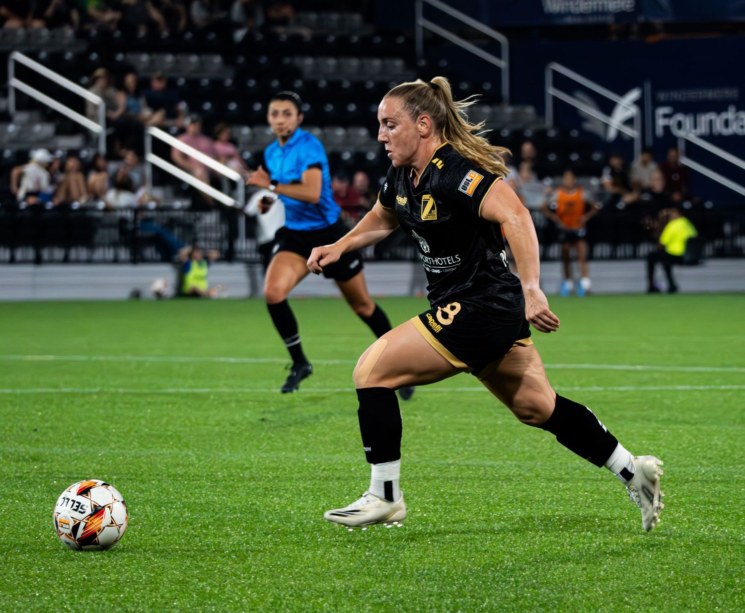 Soccer players in black uniforms stretch on a grass field before a match.