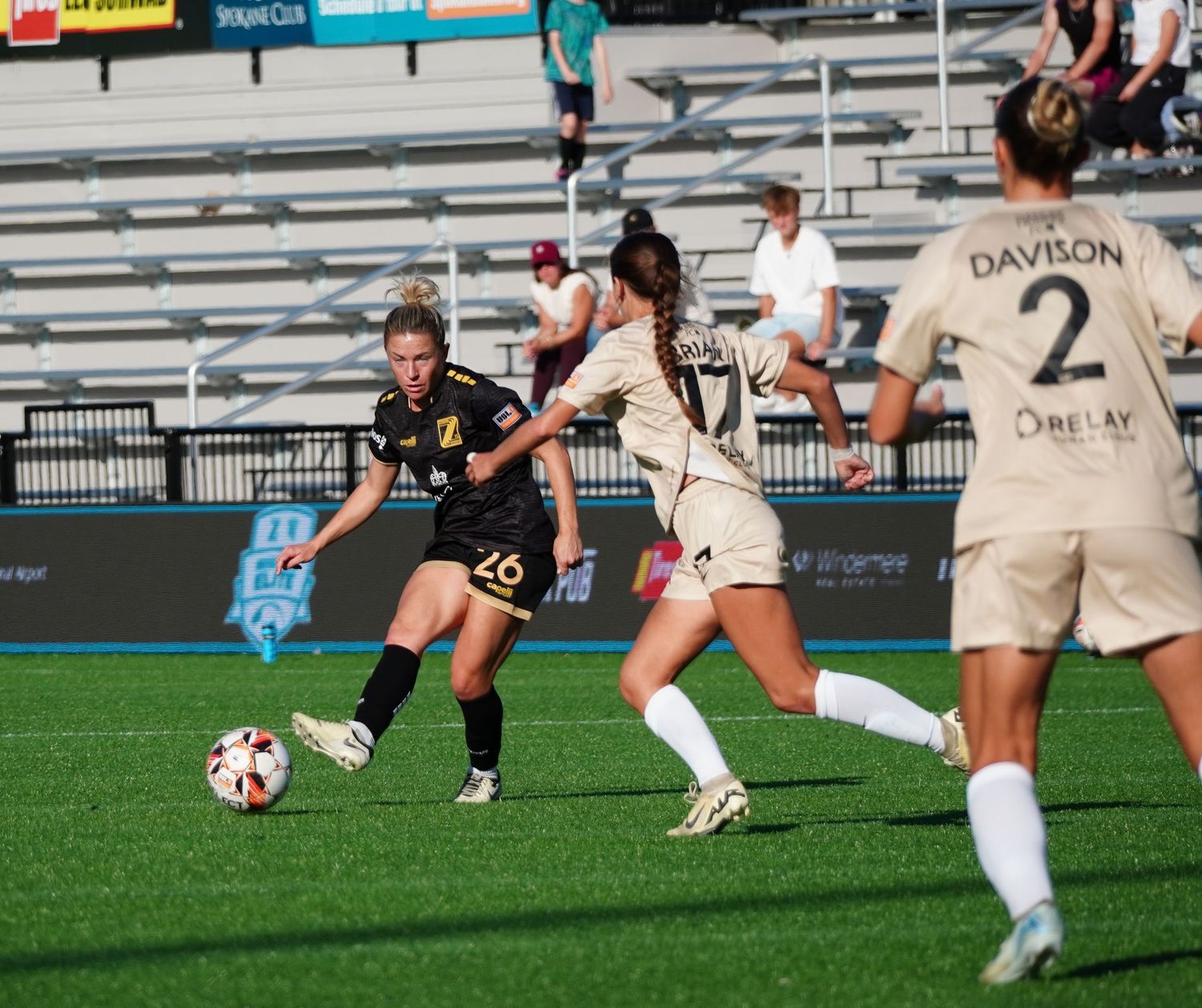 Soccer players compete for the ball during an intense match on a sunny day at a stadium field.