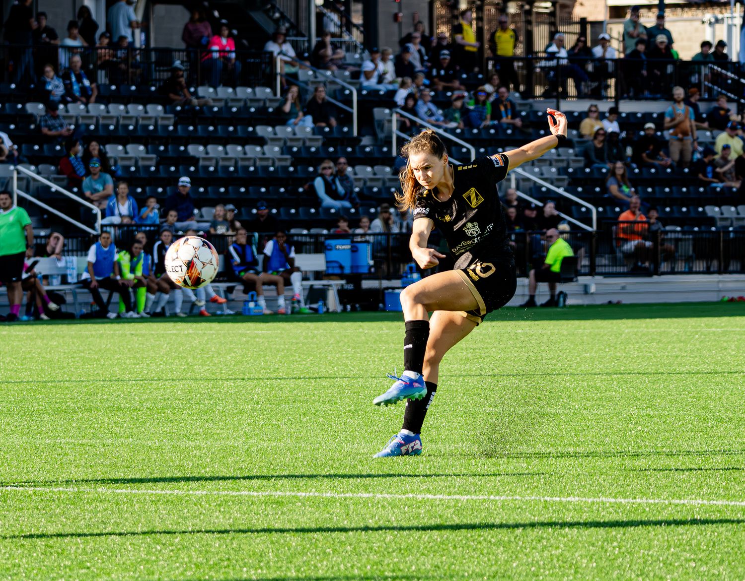 Soccer player in pink uniform kicks ball on green field during match while opponents in dark jerseys watch.