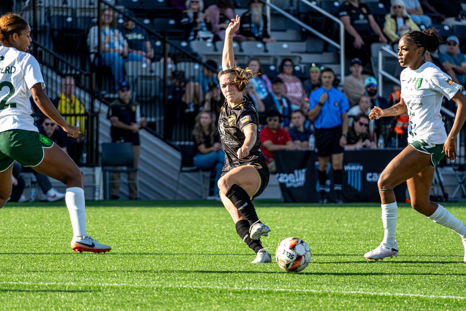 Soccer player stretches to control the ball during a competitive match on artificial turf field.