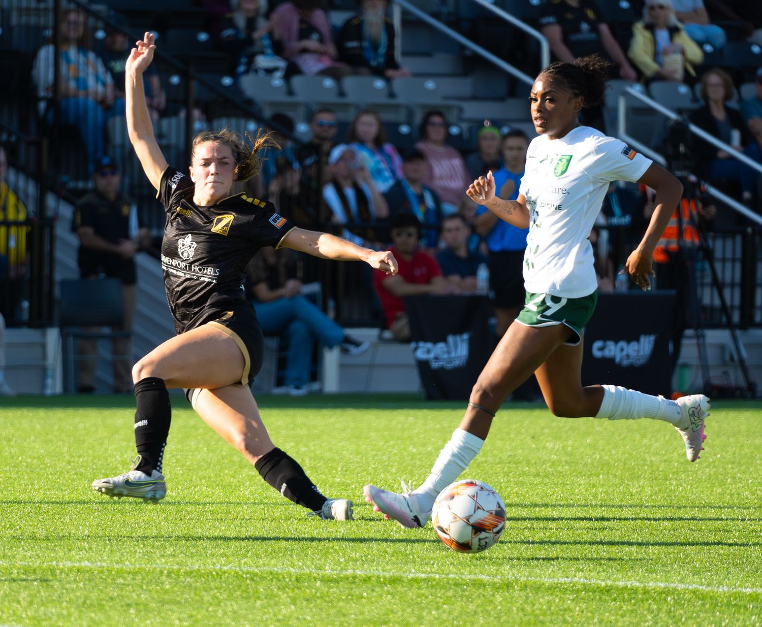 Two soccer players compete for the ball during an intense match on a sunny day at the stadium.