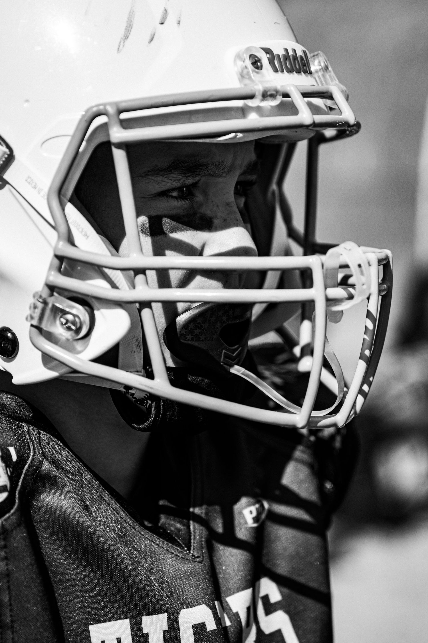 Close-up black and white photo of a football player wearing a protective helmet with face mask during a game.