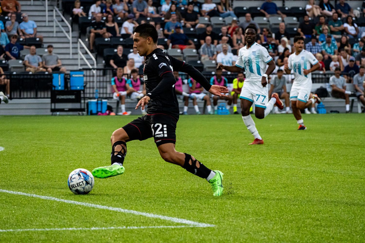 Soccer player dribbles the ball across the field during a match with teammates and opponents in view.