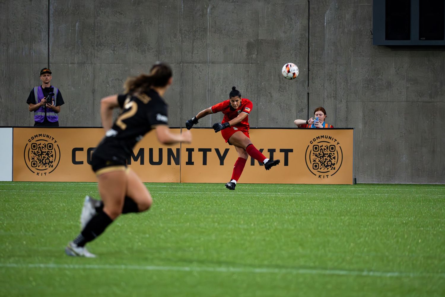 Soccer players compete on an indoor turf field with a Community First logo visible on the wall during a match.