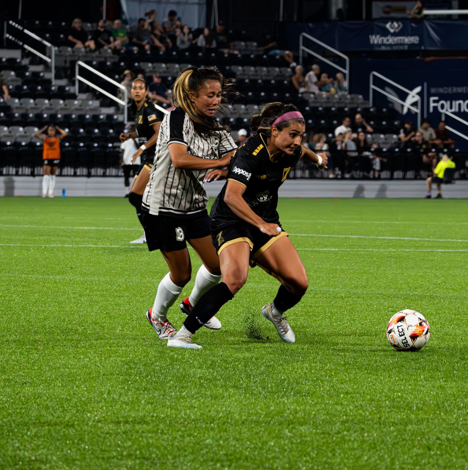 Soccer players slide across wet grass field during intense match play in stadium setting.