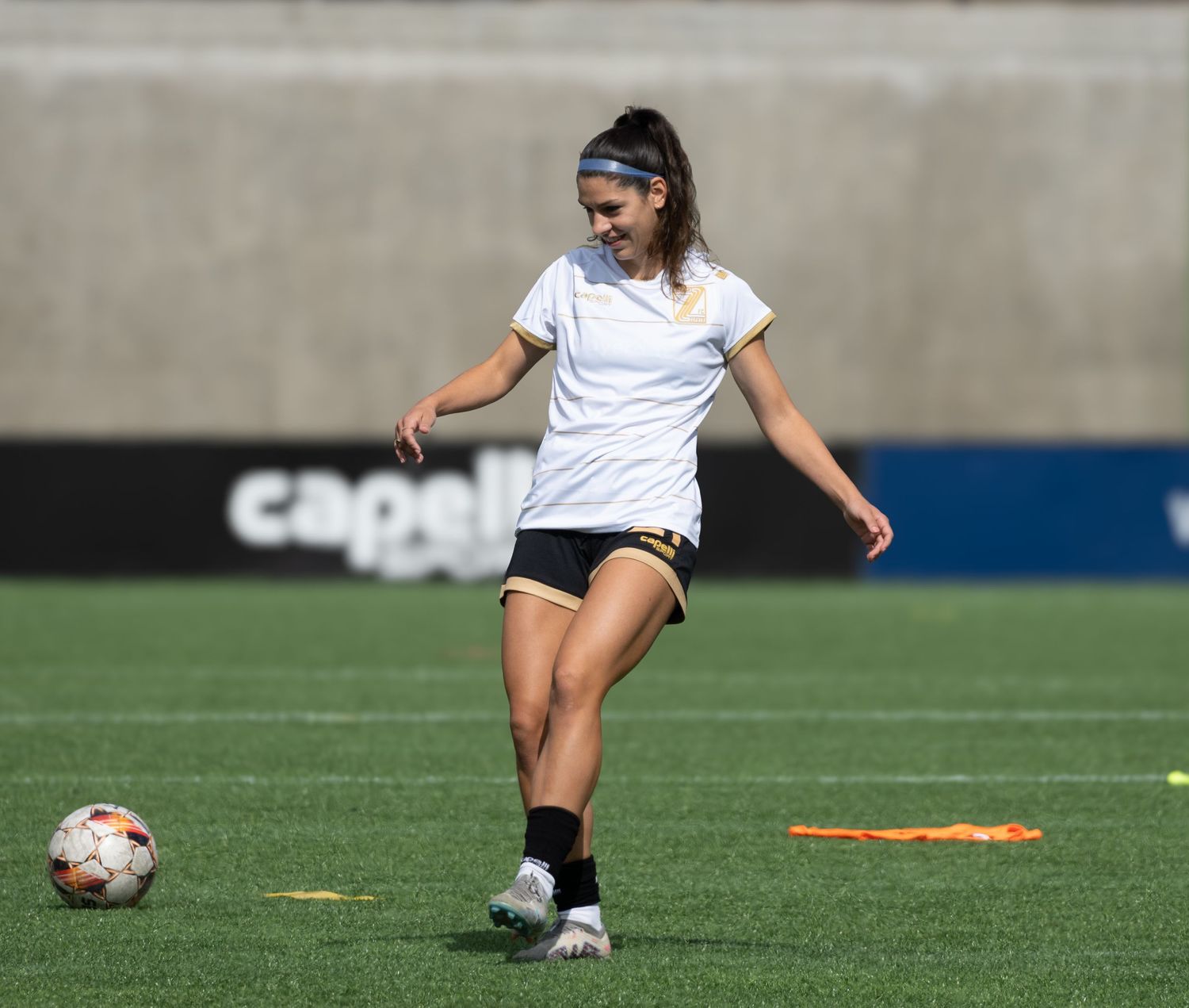 Soccer player in white jersey and black shorts prepares to kick ball during practice on artificial turf field.
