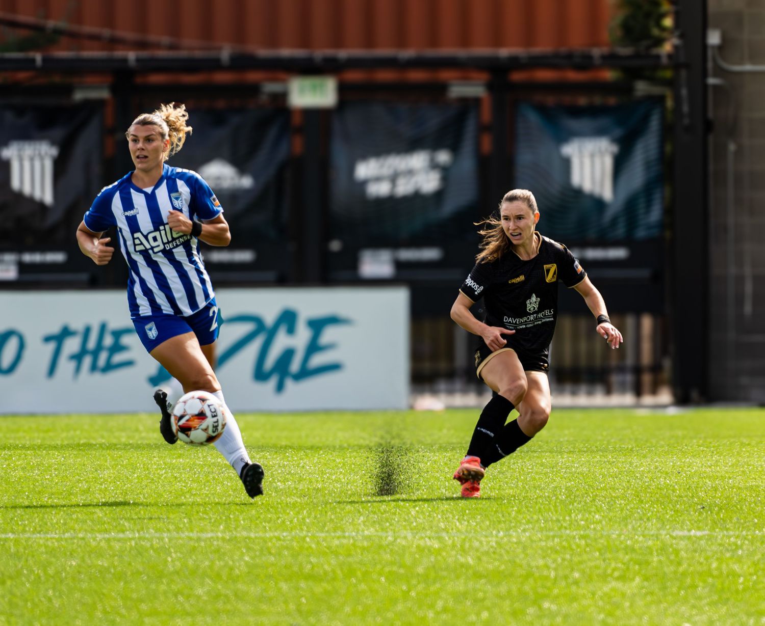 Soccer players compete for possession of the ball during an outdoor match between teams in blue and black uniforms.