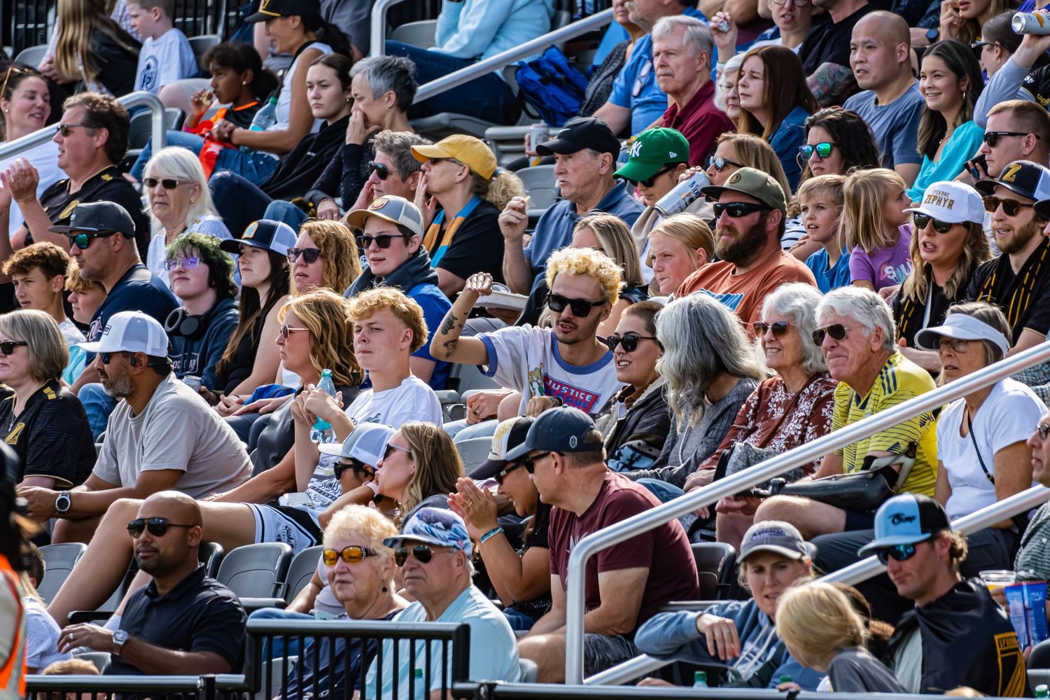 Crowded stadium bleachers filled with spectators watching a sporting event on a sunny day.