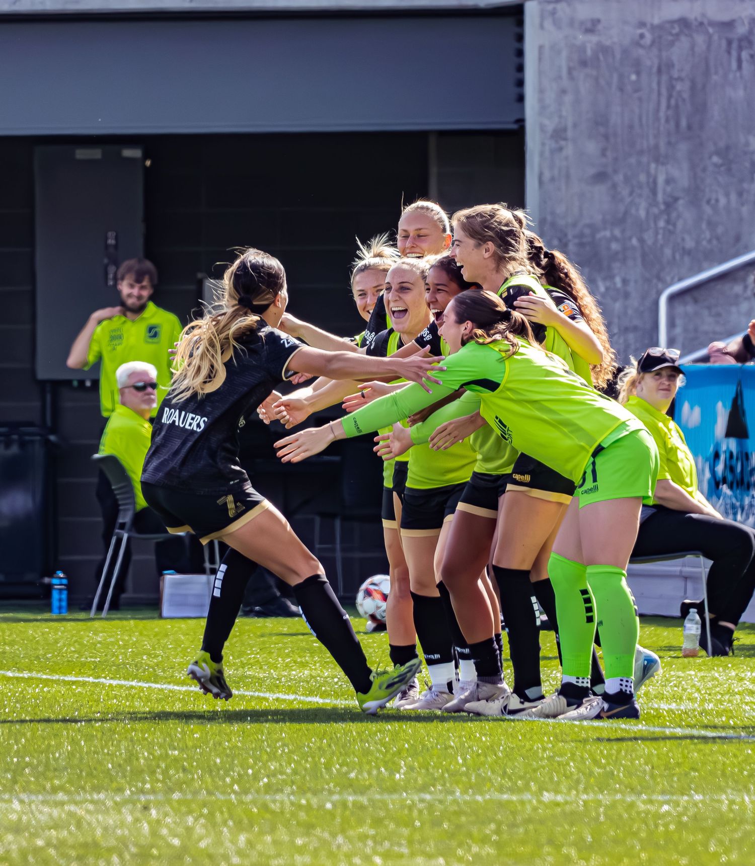 Athletes in neon yellow and black workout gear perform synchronized lunges on a sunny grass field during training.