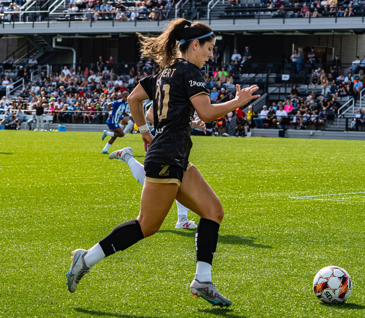 Soccer player in black uniform kicks ball on green grass field during competitive match.