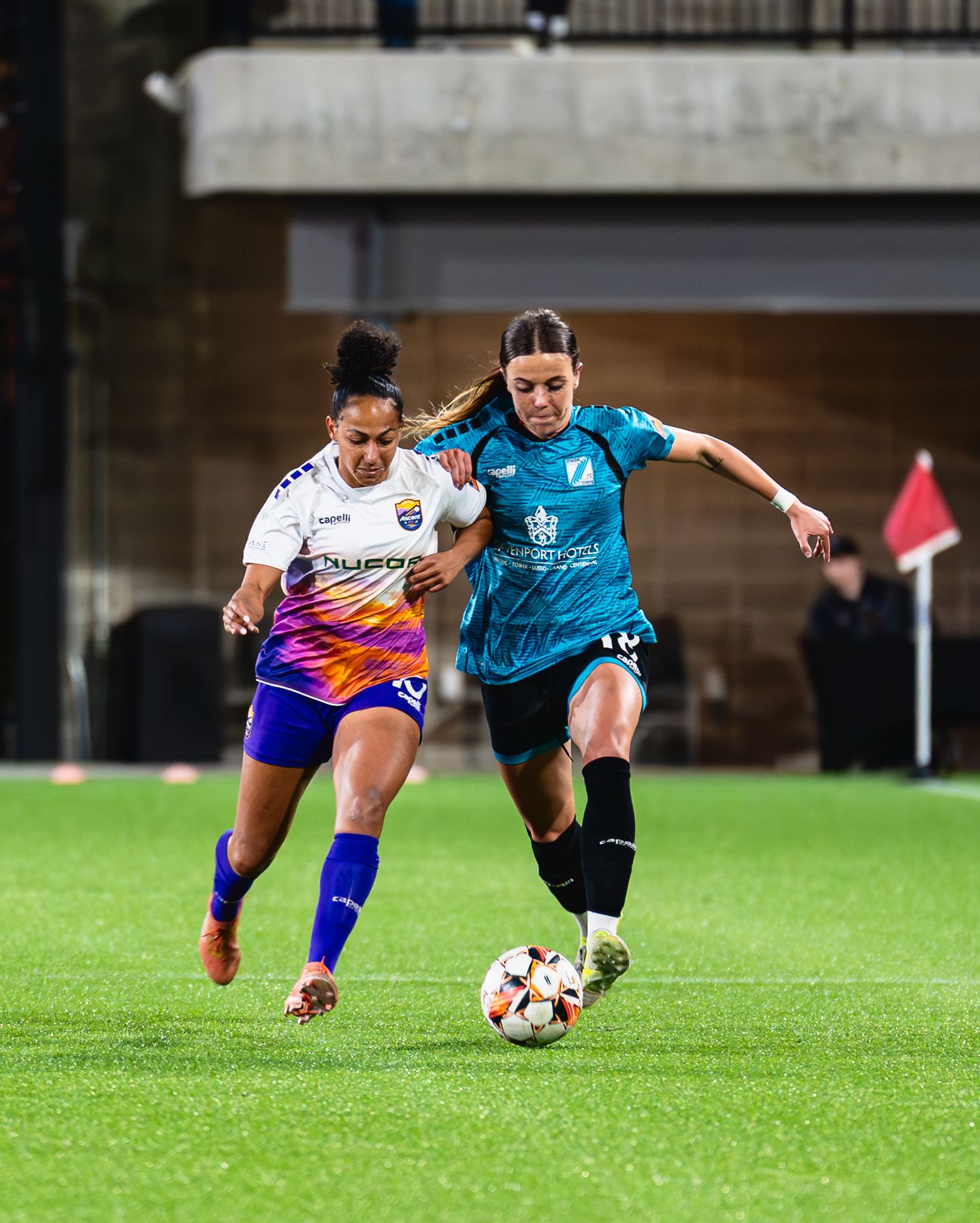 Two soccer players compete for possession of the ball during an intense match on a grass field.