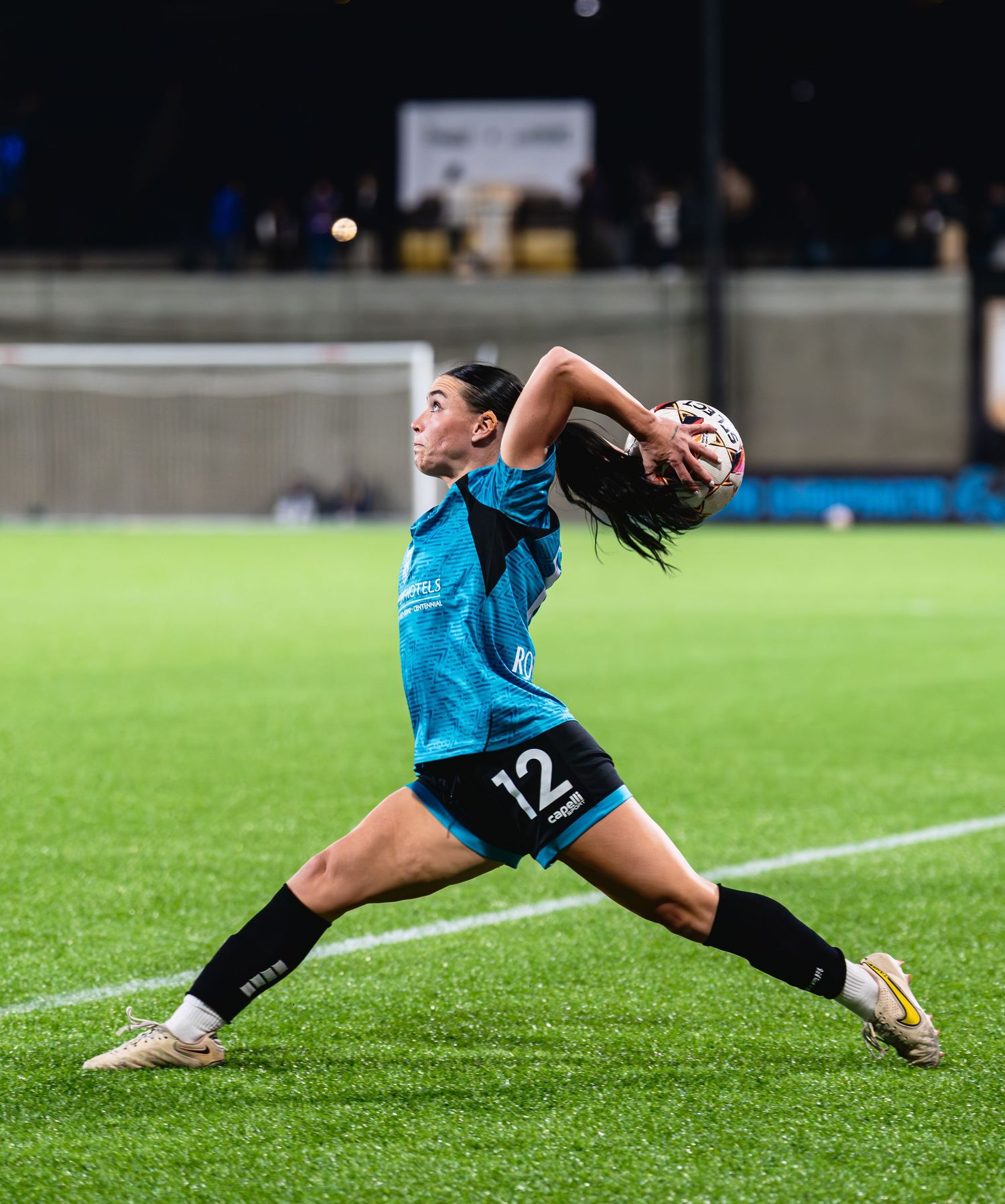 Soccer player in blue jersey diving to make a throw on grass field during match.