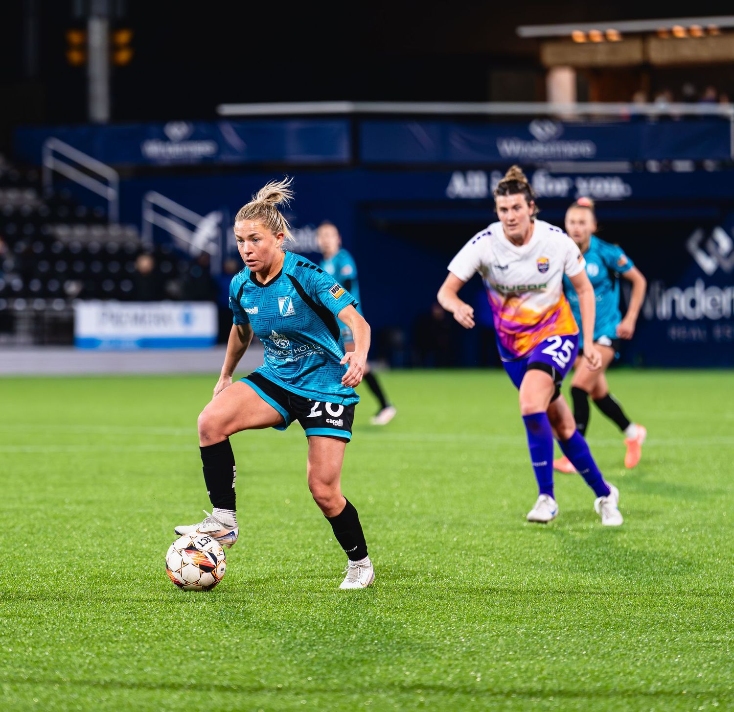 Soccer player in blue jersey dribbles ball on green grass field during competitive match.