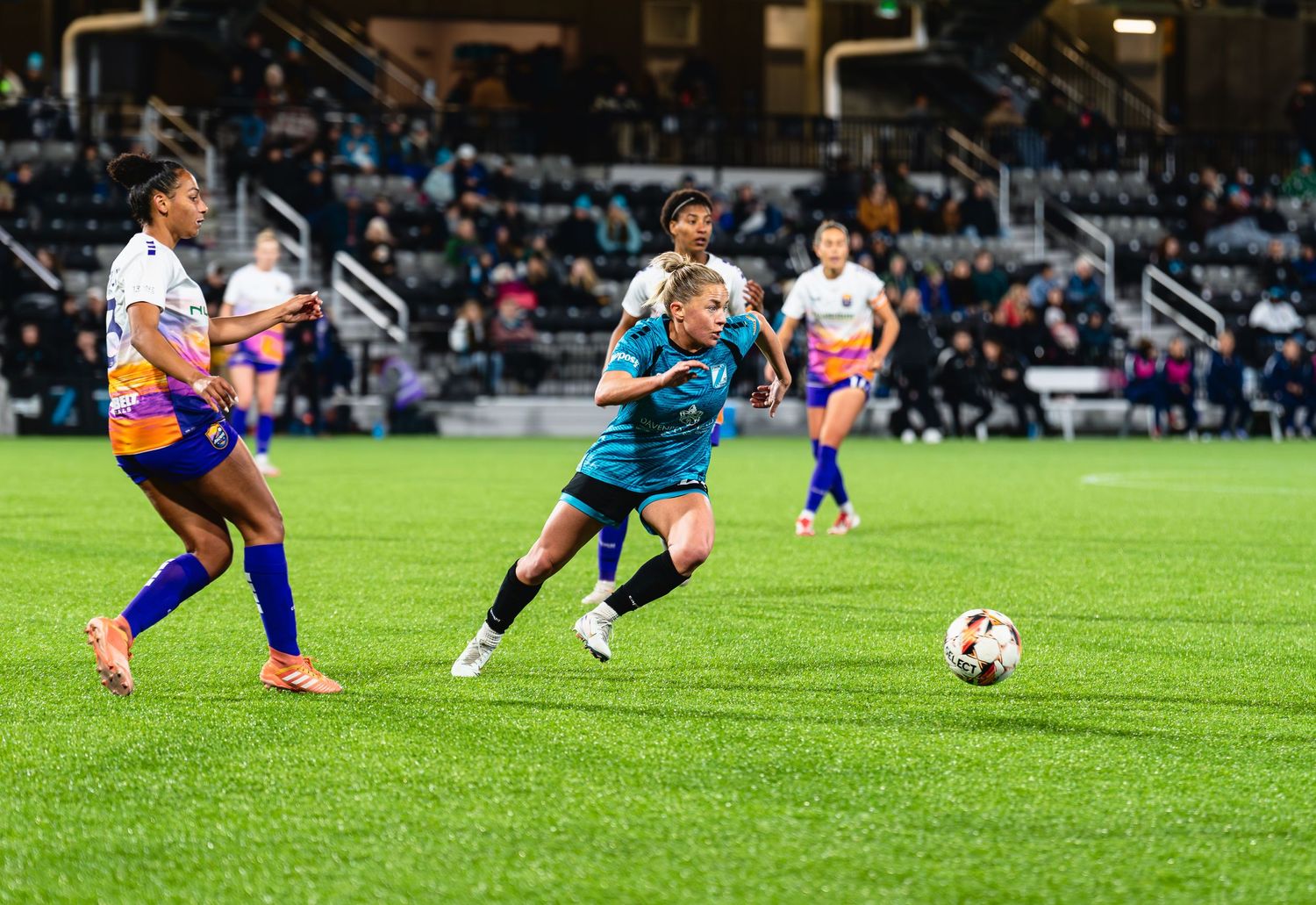 Soccer player slides across grass field attempting to block ball during competitive match.