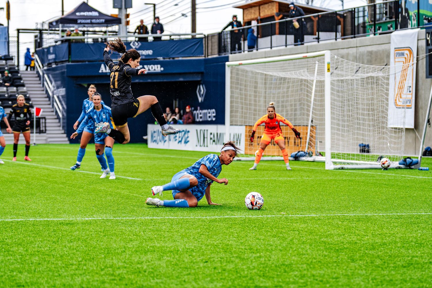 Soccer player makes a diving save to block the ball during an intense match on a grass field.