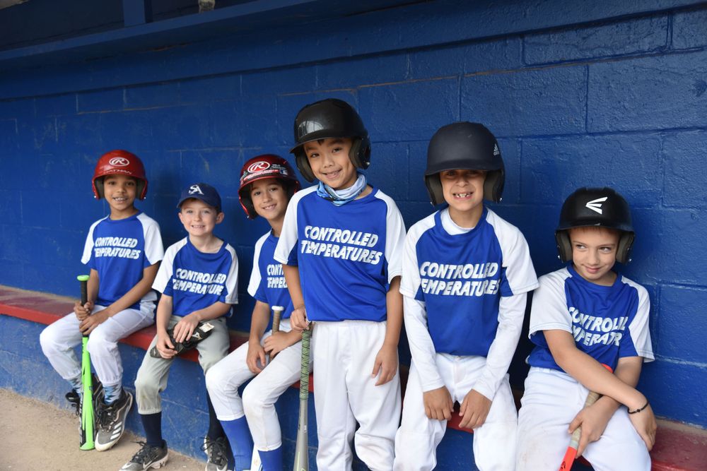 Youth baseball team players in blue and white uniforms sit in dugout.