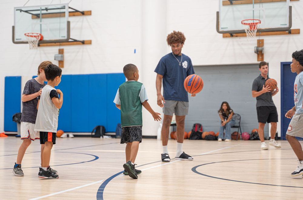 Basketball players practice drills and shooting on a court with multiple hoops in an indoor gymnasium.