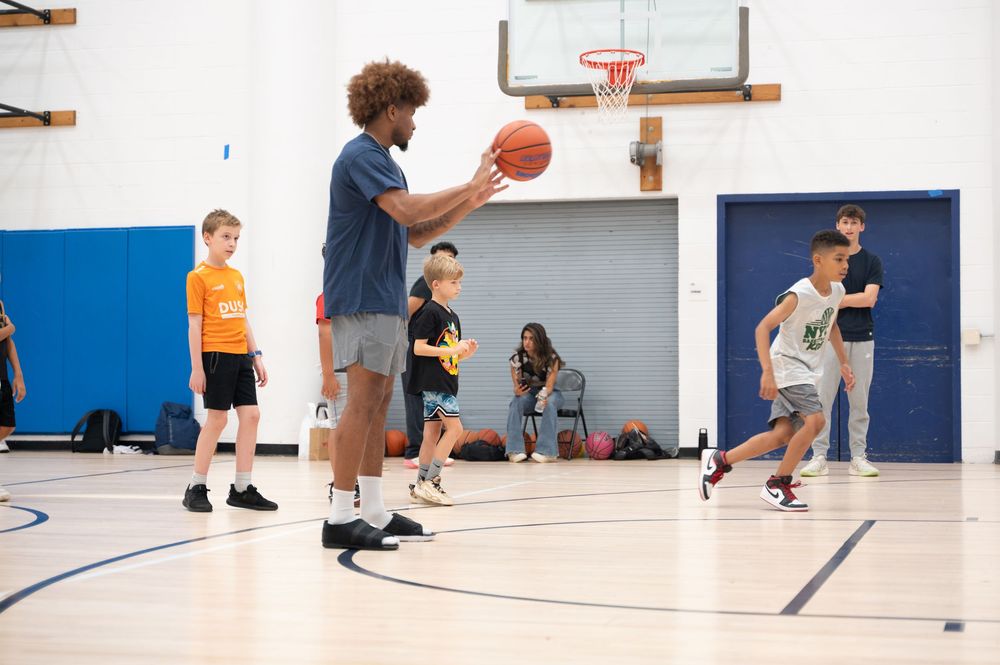 Basketball players practice dribbling drills and ball handling exercises in a blue and white indoor gymnasium.