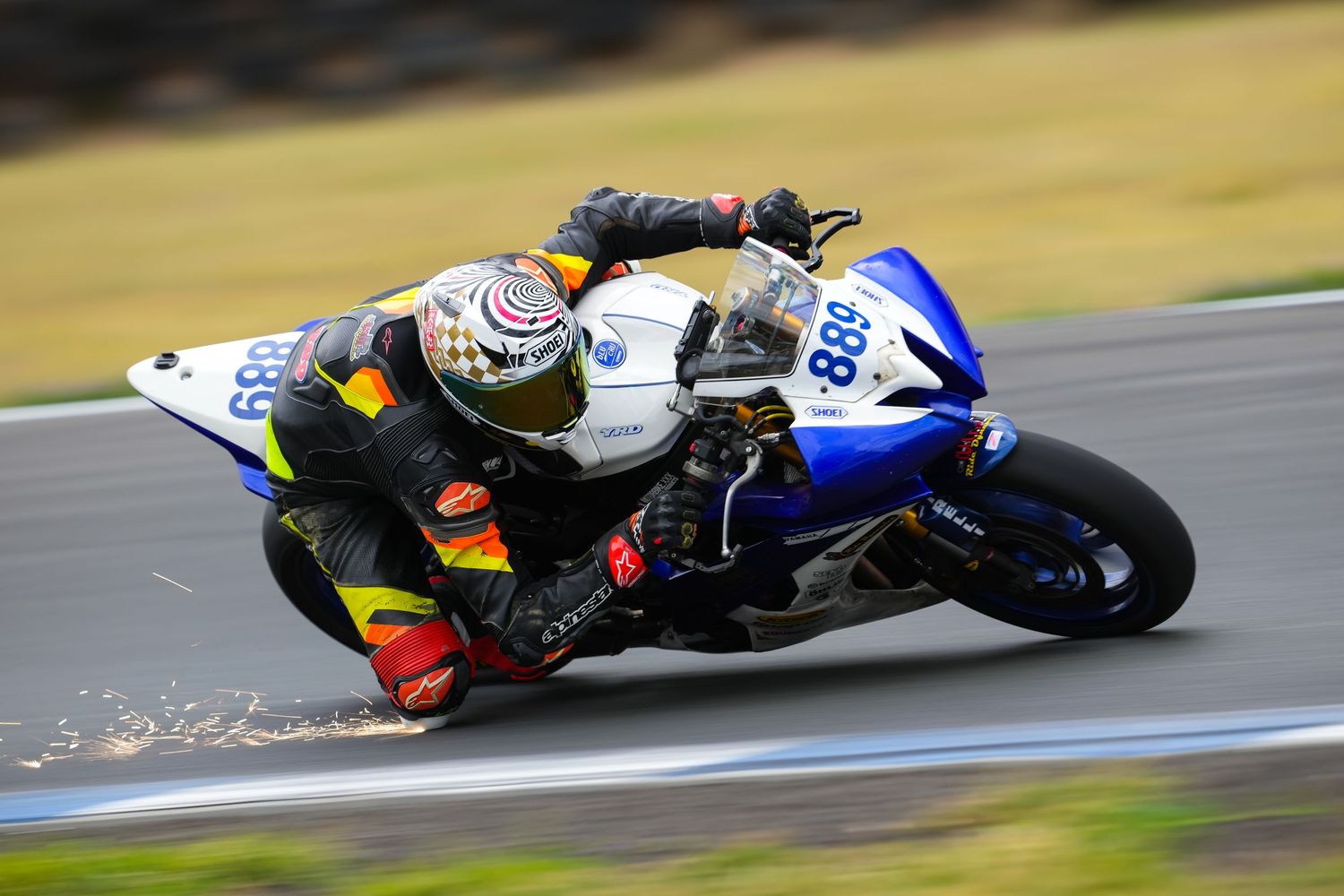 A motorcycle racer in full gear leaning hard through a racing corner.