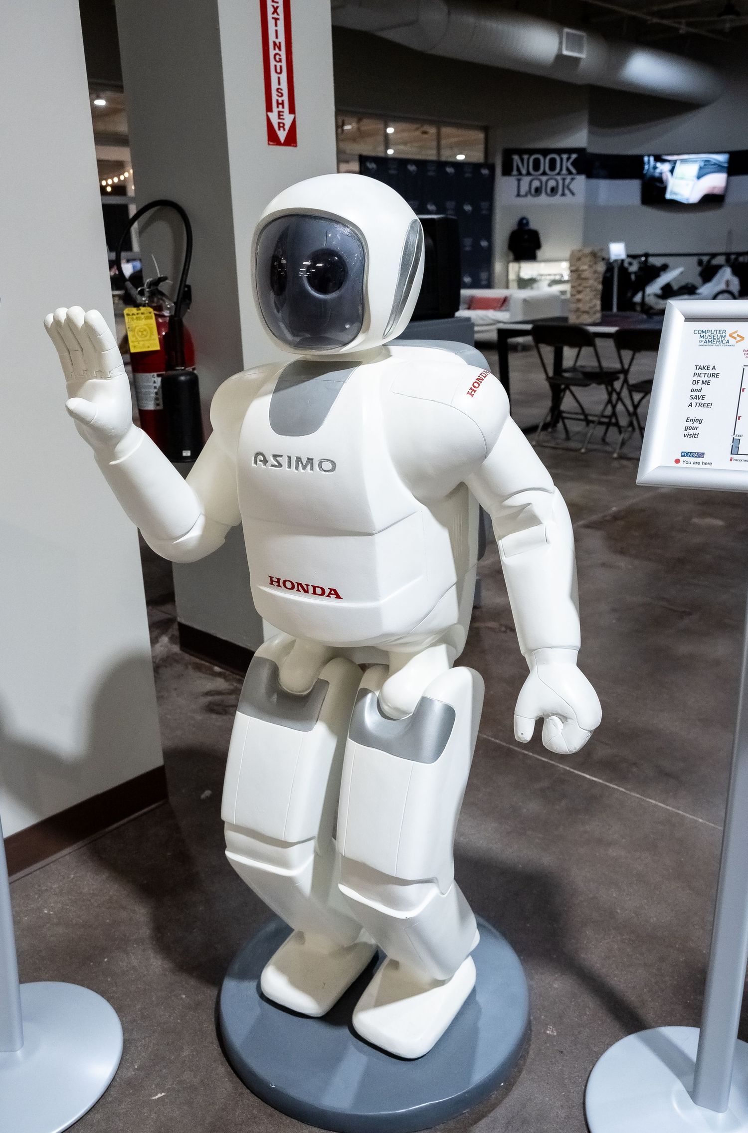 Honda's ASIMO humanoid robot standing in a museum display with a white body and raised hand.