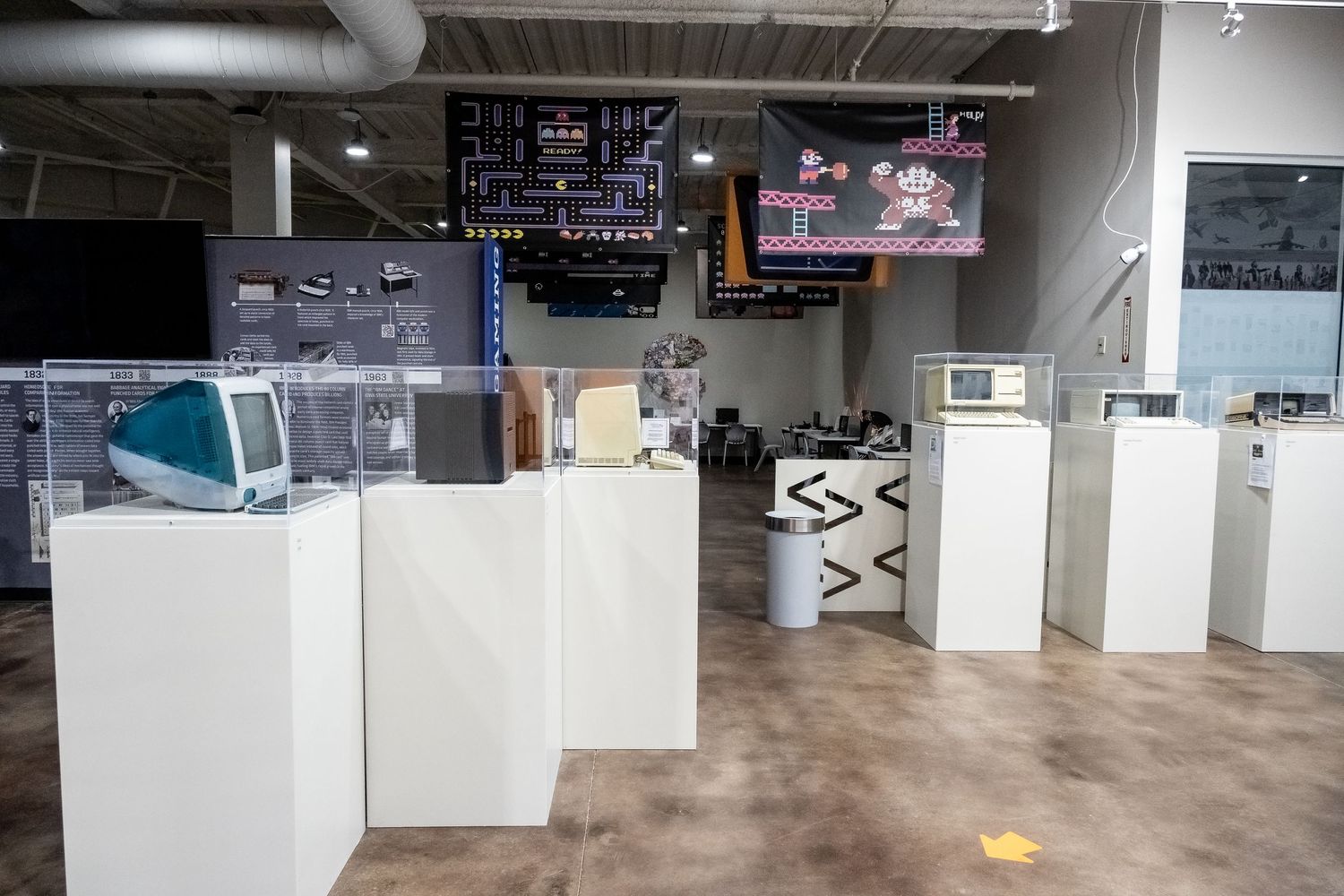 Retro gaming museum display with white pedestals showing vintage consoles and equipment.