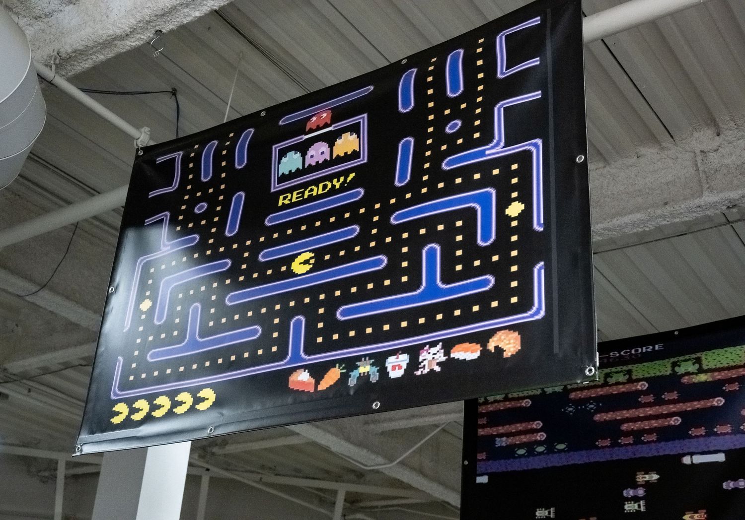 Classic Pac-Man arcade game display showing blue maze and ghosts on a large screen.