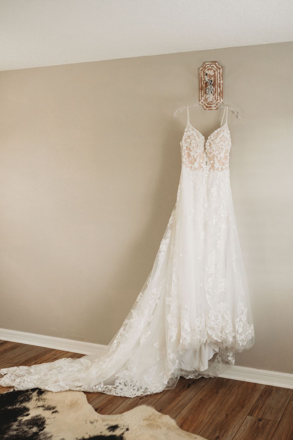 Elegant lace wedding dress hanging on display against beige wall.