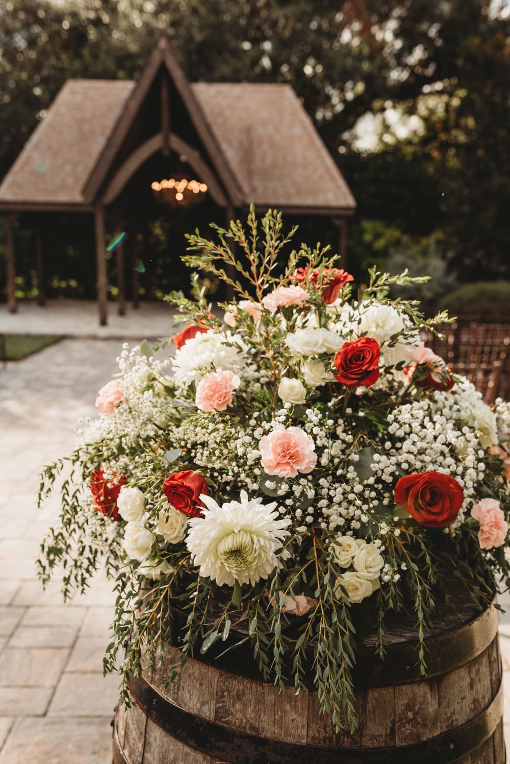 Beautiful floral arrangement with roses and baby's breath on rustic barrel with chapel in background.
