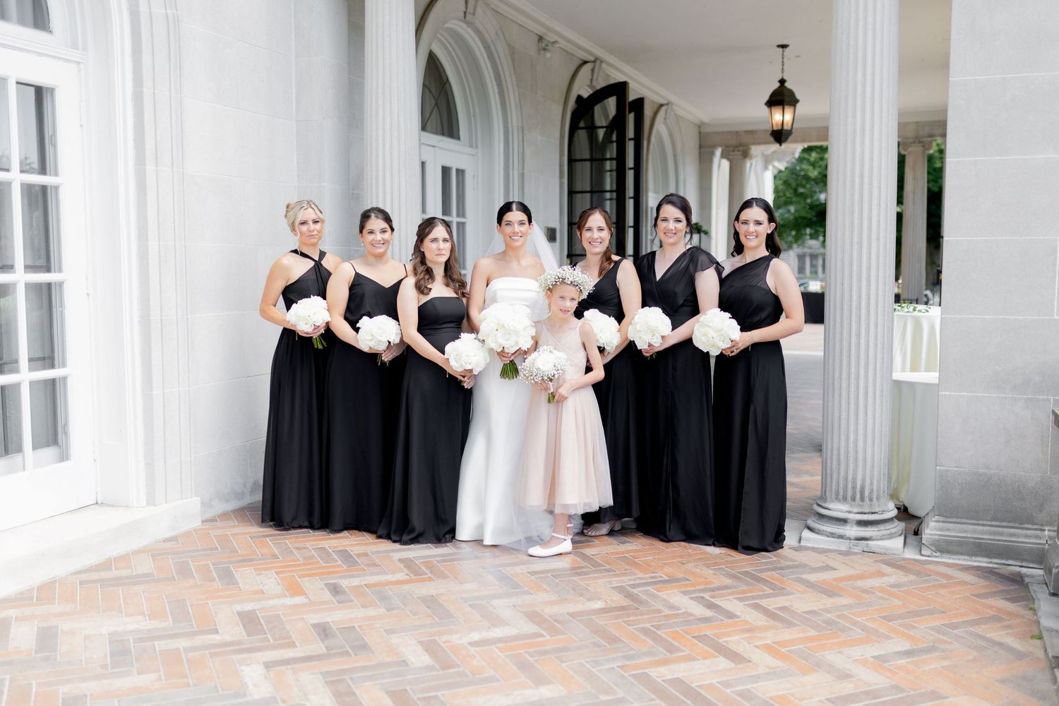 Wedding party in black and white attire posed on a grand porch with columns.