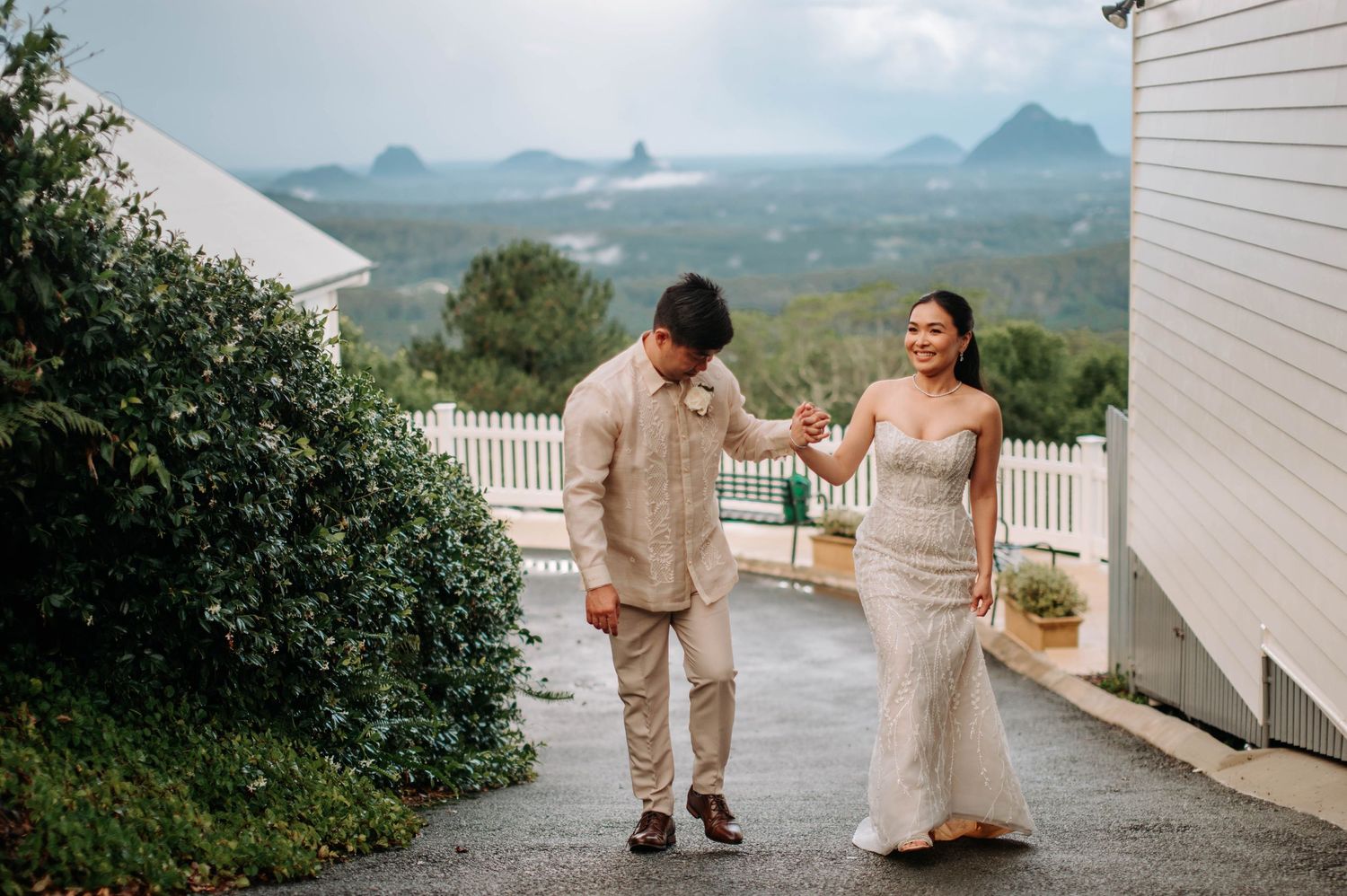 Newlyweds walking together on a pathway with mountain views in the background.
