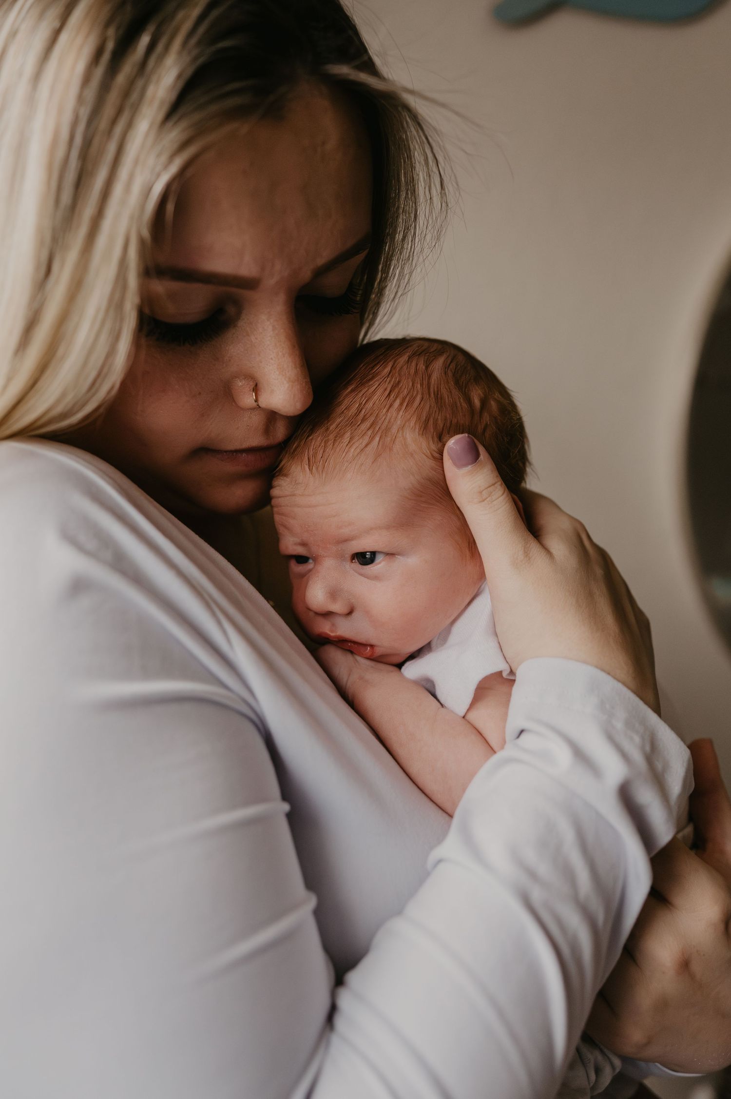 A tender moment as a blonde mother in white gently cradles her sleeping newborn baby close to her cheek.