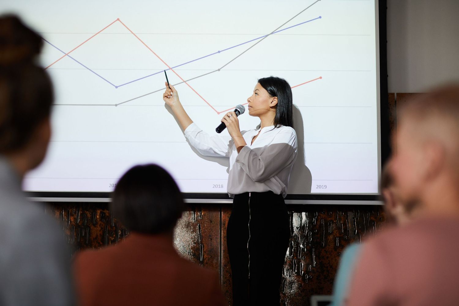 Presenter points to diagram on whiteboard during business presentation to audience.