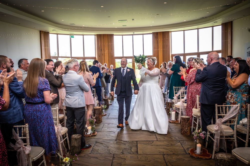 Newlyweds walk triumphantly back down the aisle as joyful wedding guests applaud in a stunning circular ceremony room.